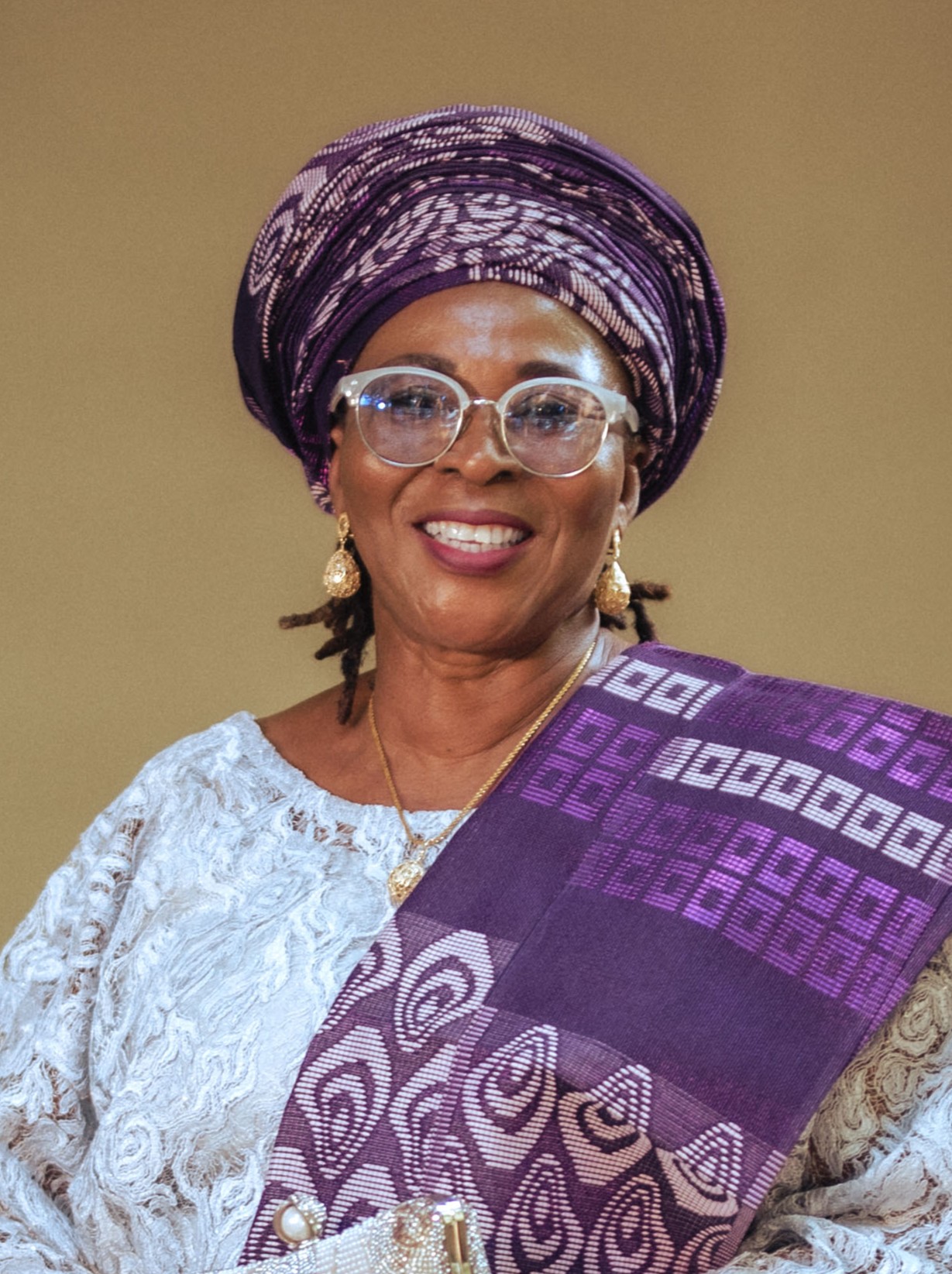 Dr. Ngozi Rosemary Akande wearing traditional Nigerian attire with purple gele and aso-oke fabric